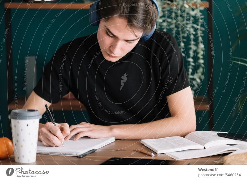 Man writing in book while listening music through headphones at home color image colour image indoors indoor shot indoor shots interior interior view Interiors