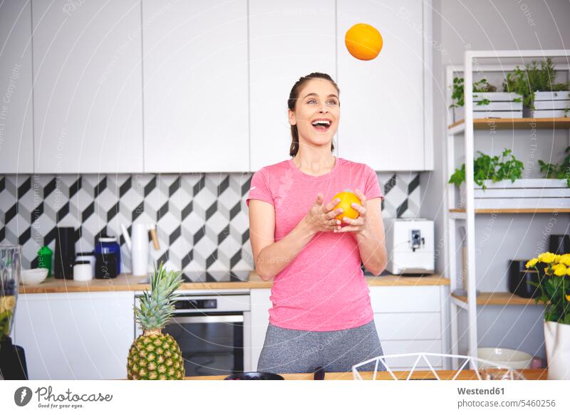 Portrait of young woman juggling with oranges in the kitchen portrait portraits Orange Citrus sinensis Oranges juggle females women domestic kitchen kitchens