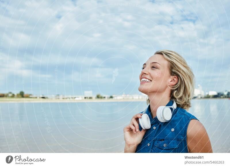 Germany, Duesseldorf, happy young woman with headphones at Rhine riverbank headset females women happiness River Rivers riverside Adults grown-ups grownups