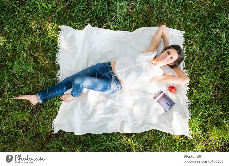 Relaxed young woman lying on picnic blanket over grass at park color image colour image Germany outdoors location shots outdoor shot outdoor shots
