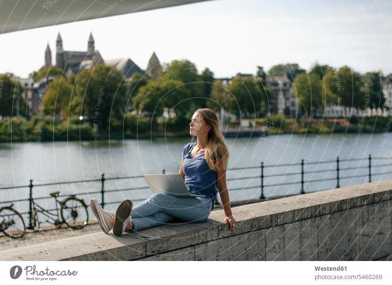 Netherlands, Maastricht, young woman sitting on a wall at the riverside with laptop females women Laptop Computers laptops notebook River Rivers Seated