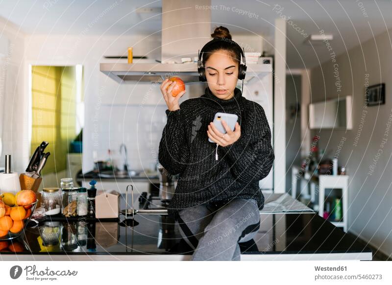 Teenage girl wearing headphone holding apple while using mobile phone at home color image colour image indoors indoor shot indoor shots interior interior view