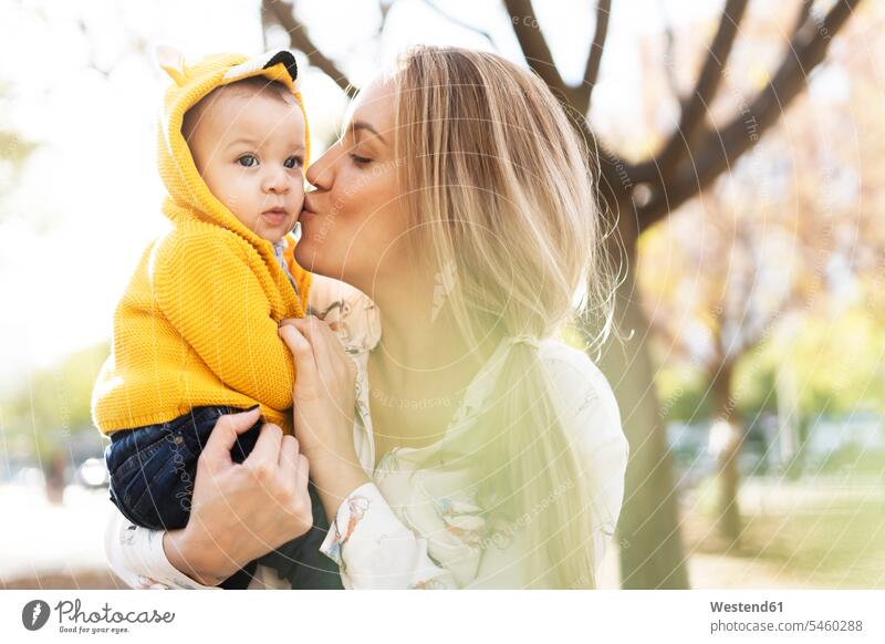 Mother kissing baby boy in a park coat coats jackets hold cuddle snuggle snuggling kisses embrace Embracement hug hugging delight enjoyment Pleasant pleasure