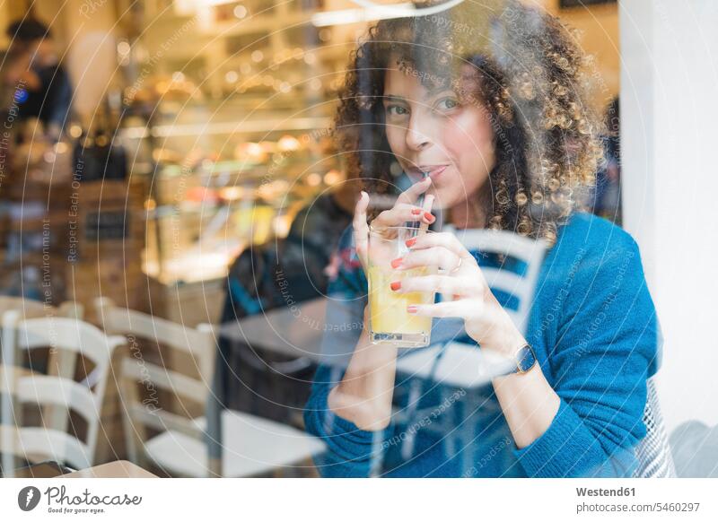 Portrait of woman drinking a smoothie behind windowpane in a cafe human human being human beings humans person persons curl curled curls curly hair windows