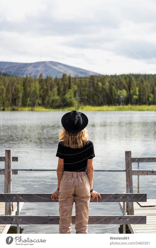Finland, Lapland, woman wearing a hat standing on jetty at a lake lakes hats jetties females women water waters body of water Adults grown-ups grownups adult