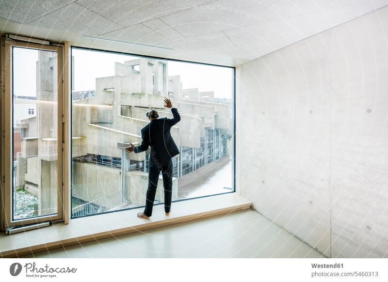 Back view of barefoot businessman with Virtual Reality Glasses standing on window sill looking out of window Businessman Business man Businessmen Business men