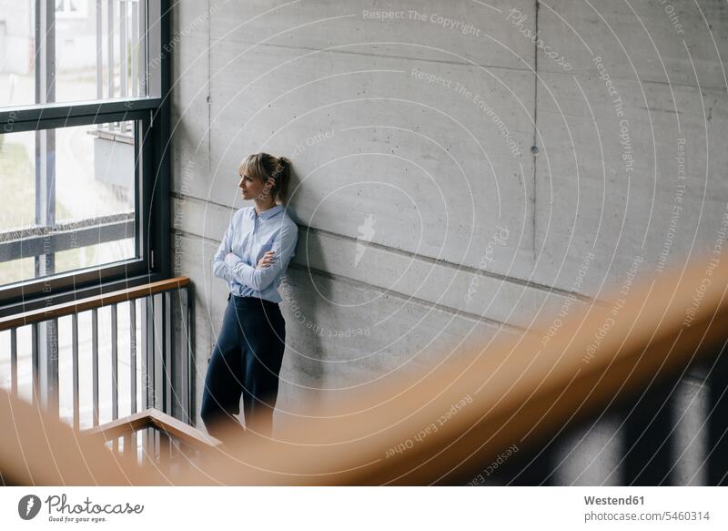 Successful businesswoman leaning on wall, looking out of window, with arms crossed manager female managers Railing Railings standing businesswomen