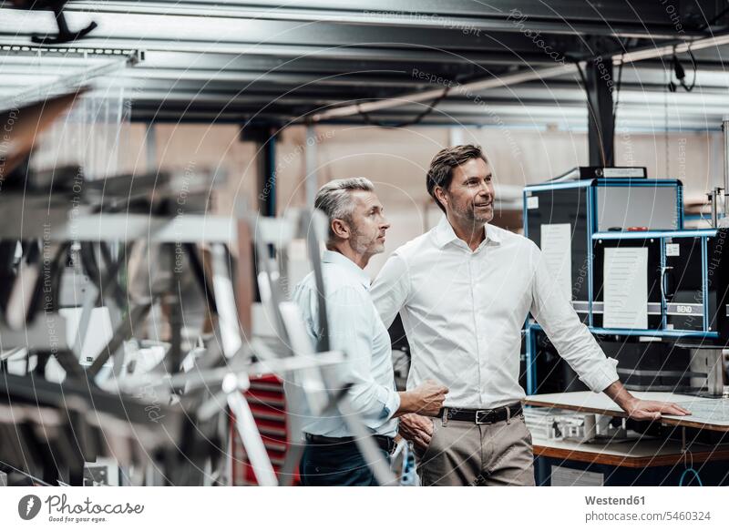 Mature colleague discussing with smiling manager while standing by manufacturing machinery in factory color image colour image Germany indoors indoor shot