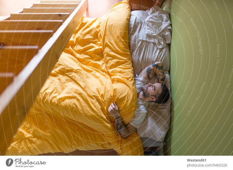 Tattooed man lying in bed, wooden ladder human human being human beings humans person persons caucasian appearance caucasian ethnicity european adult grown-up