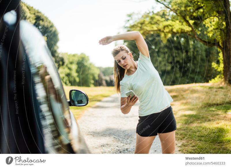 Sportive young woman stretching and using cell phone at a car in a park automobile Auto cars motorcars Automobiles parks mobile phone mobile phones Cellphone