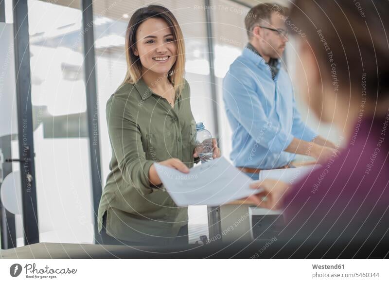 Smiling businesswoman in office handing over paper to colleague document documents papers businesswomen business woman business women offices office room