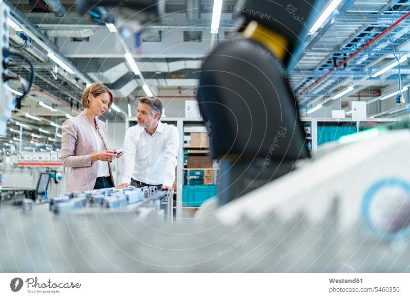 Businessman and businesswoman talking in a modern factory hall business life business world business person businesspeople associate associates