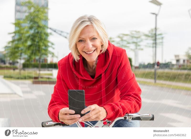 Portrait of smiling senior woman with city bike and cell phone bicycle bikes bicycles portrait portraits smile confidence confident females women mobile phone