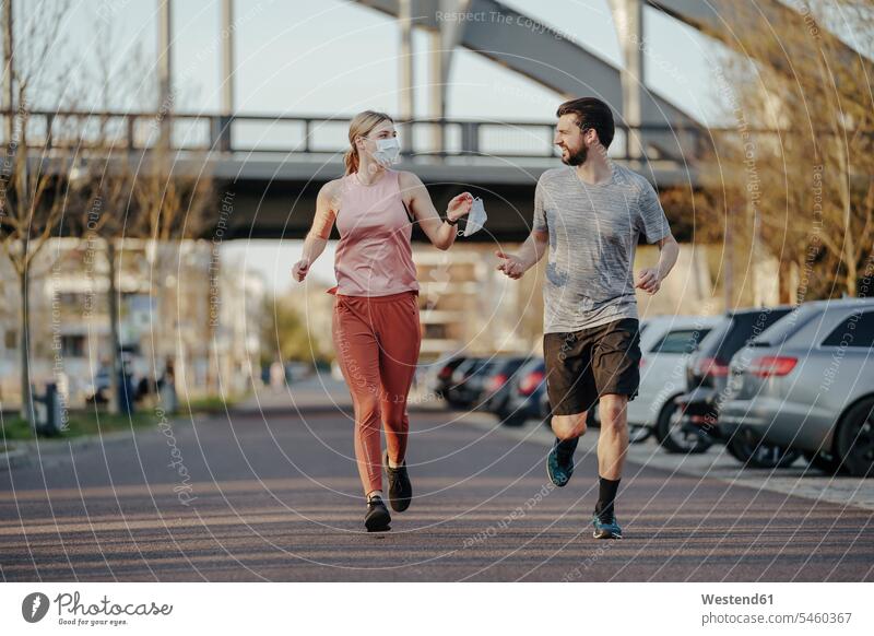Young woman jogging while giving man face mask during COVID-19 pandemic color image colour image outdoors location shots outdoor shot outdoor shots day