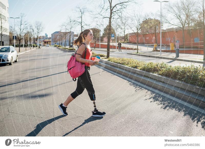 Sporty young woman with leg prosthesis walking in the city back-pack back-packs backpacks rucksack rucksacks exercise practising train training go going colour