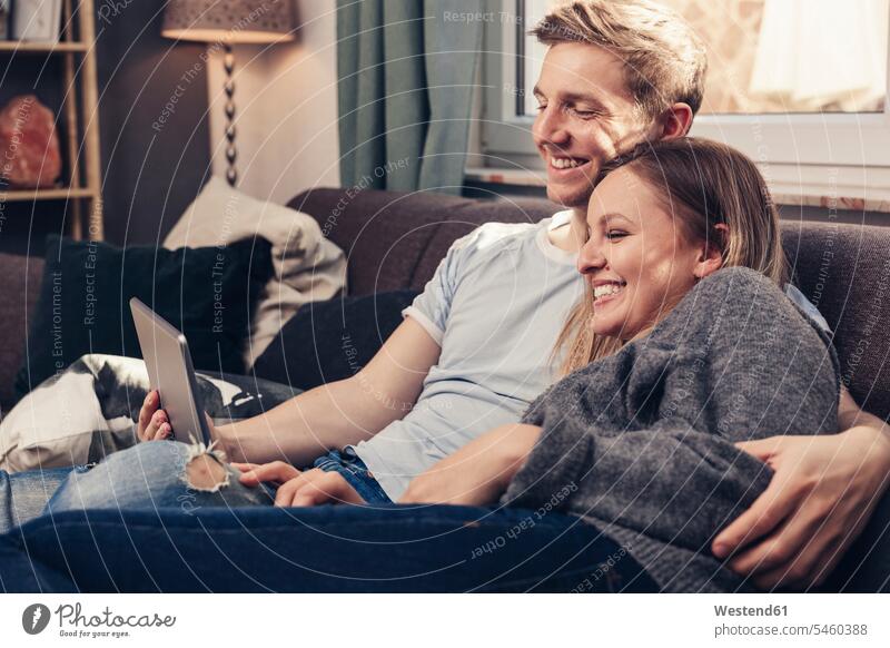 Happy young couple using tablet on couch at home relaxed relaxation twosomes partnership couples settee sofa sofas couches settees digitizer Tablet Computer