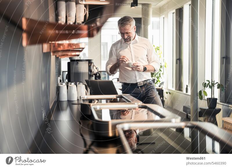 Smiling mature businessman looking at laptop in office kitchen smiling smile Businessman Business man Businessmen Business men domestic kitchen kitchens offices