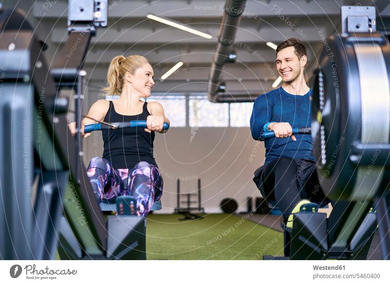 Man and woman at gym exercising together on rowing machines gyms Health Club men males females women Rowing Machines fitness Adults grown-ups grownups adult