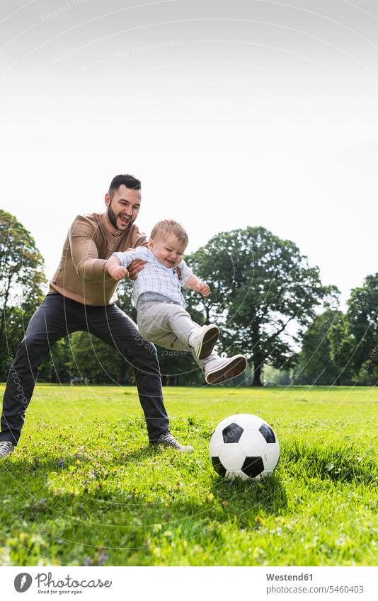 Happy father playing football with son in a park sons manchild manchildren parks happiness happy active fathers daddy dads papa soccer family families people