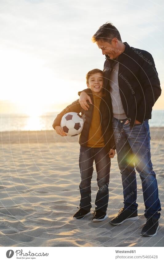 Father embracing son with football on the beach at sunset beaches sunsets sundown embrace Embracement hug hugging father pa fathers daddy dads papa soccer ball