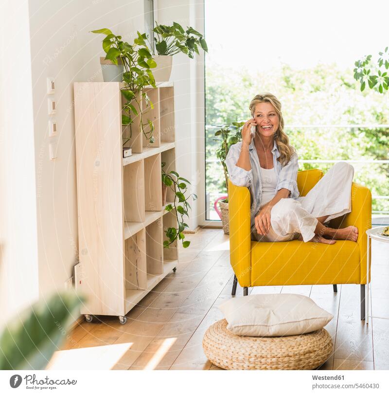 Portrait of laughing mature woman on the phone relaxing in armchair at home cushions rack racks Shelve shelves telecommunication phones telephone telephones