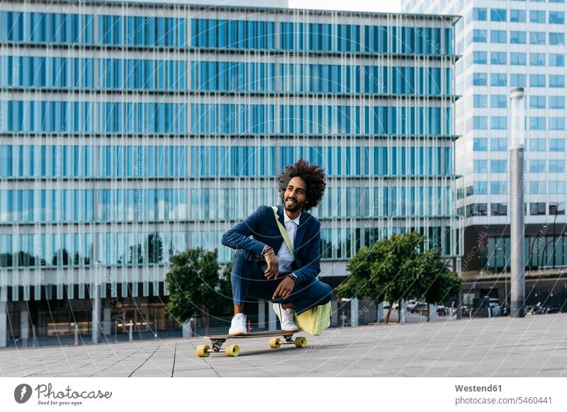 Spain, Barcelona, young businessman crouching on skateboard in the city Businessman Business man Businessmen Business men town cities towns males cowering