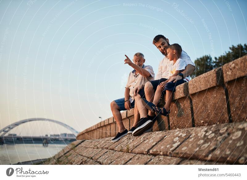 Grandfather, father and son sitting on a wall at the riverside human human being human beings humans person persons caucasian appearance caucasian ethnicity
