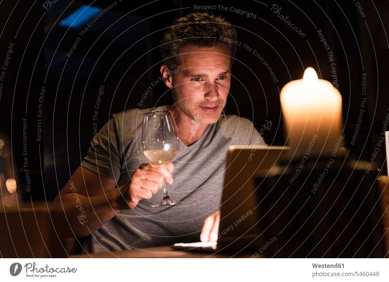 Man having glass of white wine looking at laptop Wine Laptop Computers laptops notebook eyeing man men males Dinner Alcohol alcoholic beverage Alcoholic Drink