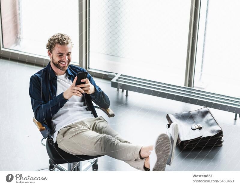 Smiling casual businessman sitting in office with feet up using cell phone mobile phone mobiles mobile phones Cellphone cell phones offices office room