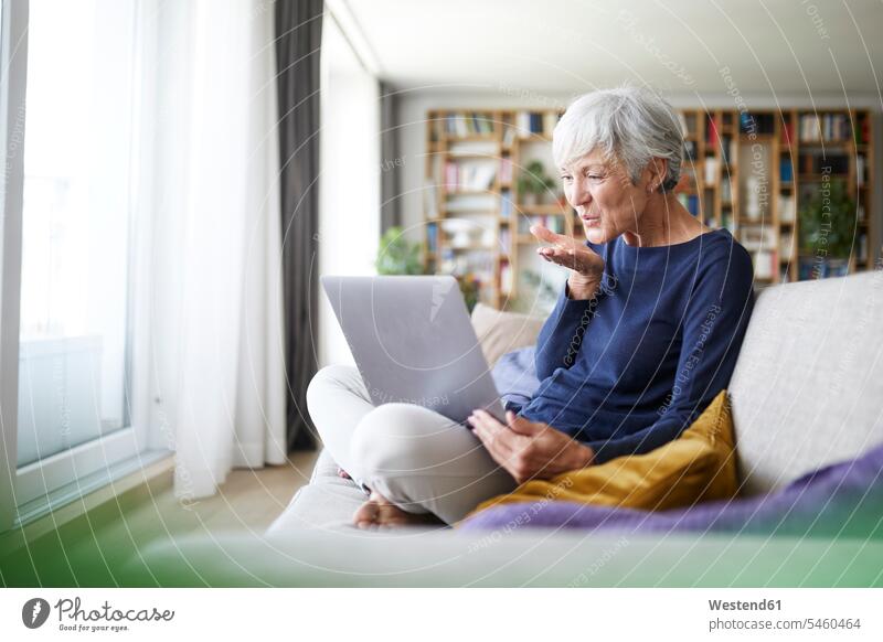 Senior woman giving flying kiss on video call while sitting at home color image colour image indoors indoor shot indoor shots interior interior view Interiors