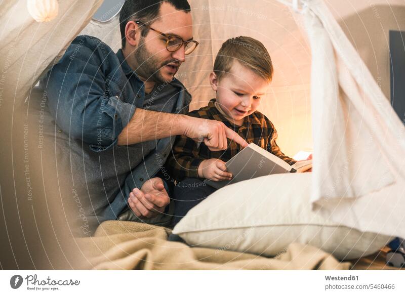 Father and son reading a book together in tent at home books tents sons manchild manchildren father pa fathers daddy dads papa family families people persons