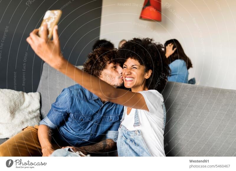 Happy couple sitting on couch taking a selfie Selfie Selfies Seated happiness happy twosomes partnership couples settee sofa sofas couches settees people