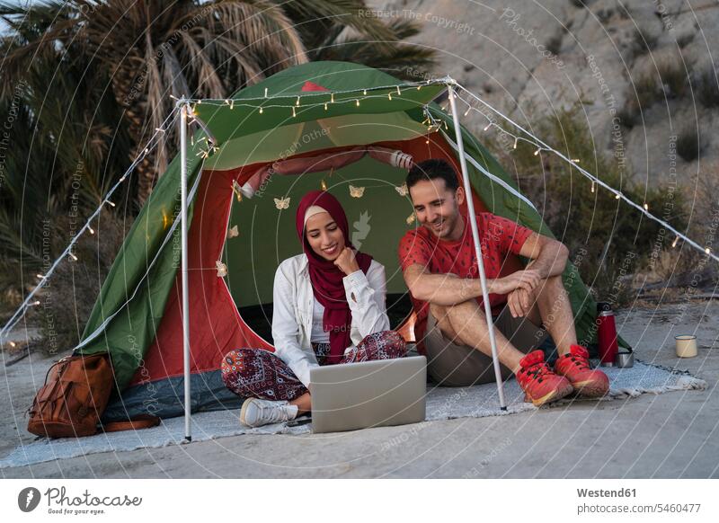 Young woman wearing Hijab and man using laptop at a tent head cloth head cloths head scarf head scarves headscarves computers Laptop Computer Laptop Computers