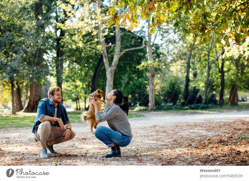 Happy young couple with dog in a park animals creature creatures domestic animal pet Canine dogs relax relaxing hold kiss kisses smile delight enjoyment