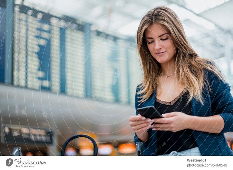 Young woman using cell phone at departure board looking around mobile phone mobiles mobile phones Cellphone cell phones females women departures board