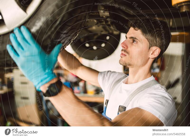 Mechanic working on the underbody of a car in a workshop mechanic mechanician repairman mechanicians mechanists repairmen mechanics machinists At Work