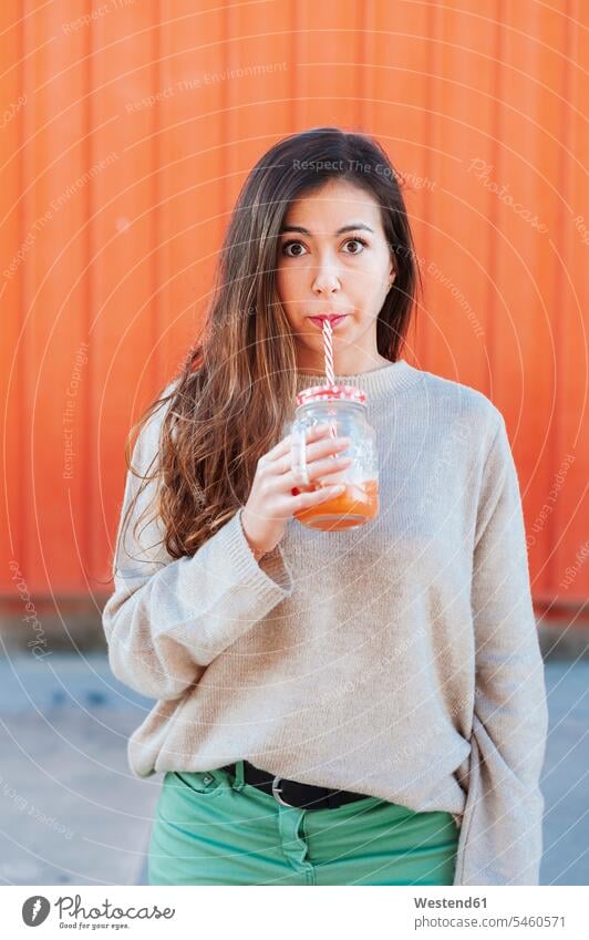 Beautiful woman drinking juice while standing against orange wall color image colour image outdoors location shots outdoor shot outdoor shots day daylight shot