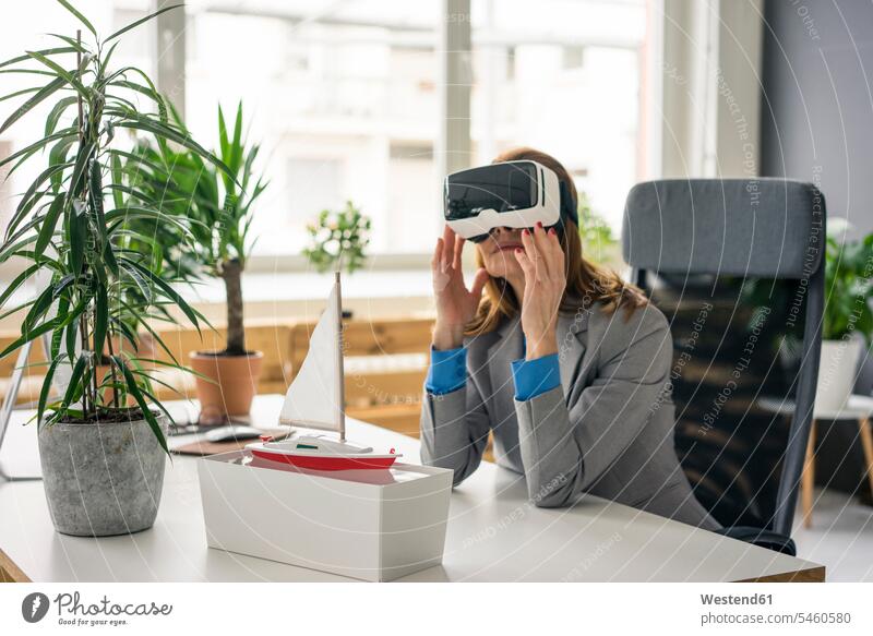 Businesswoman sitting at desk with a ship model, looking through VR glasses Virtual Reality Glasses Virtual-Reality Glasses virtual reality headset vr headset