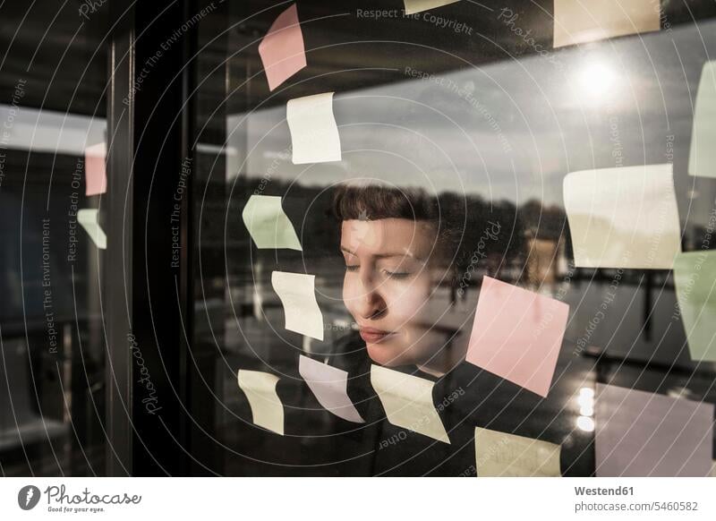 Tired woman leaning against window pane with sticky notes businesswoman businesswomen business woman business women Post it Post-it eyes closed closed eyes