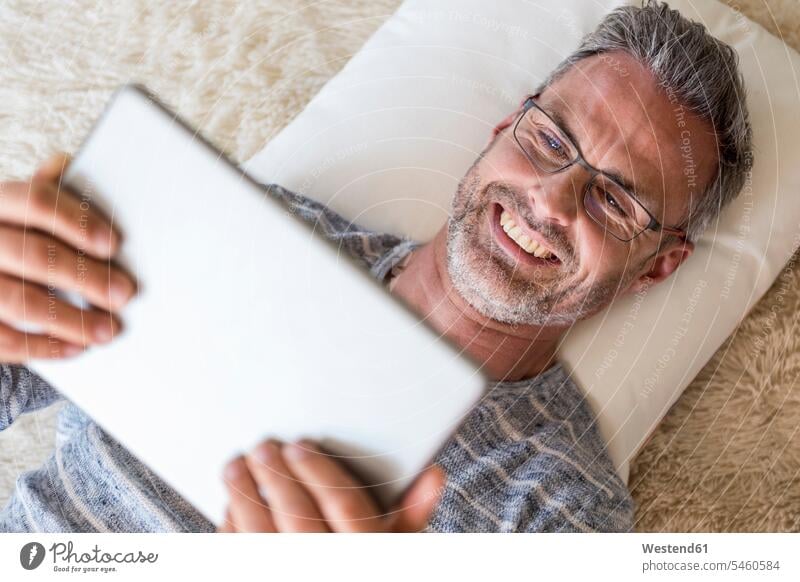 Mature man lying on pillow using a tablet laying down lie lying down men males digitizer Tablet Computer Tablet PC Tablet Computers iPad Digital Tablet
