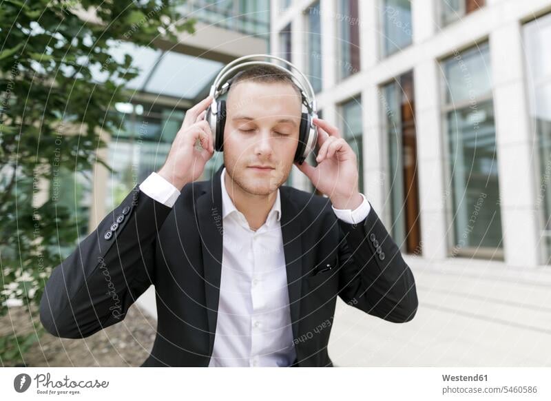 Young businessman with closed eyes wearing headphones outdoors headset Businessman Business man Businessmen Business men males business people businesspeople