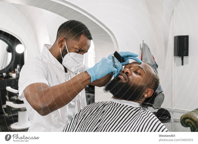 Man with full beard getting a shave, barber wearing surgical mask and gloves human human being human beings humans person persons client clientele clients