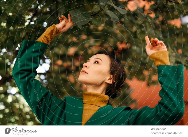 Close-up of young woman looking at leaves growing on tree color image colour image Spain casual clothing casual wear leisure wear casual clothes Casual Attire