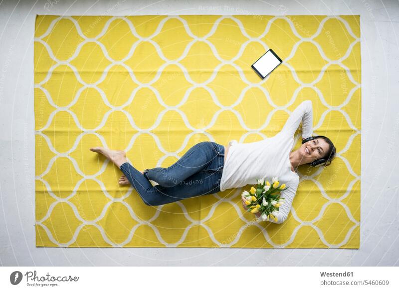 Smiling woman wearing headphones lying on carpet with bunch of tulips Bunch of Flowers Bouquet Flower Bouquet Bouquet of Flowers Flower Bouquets