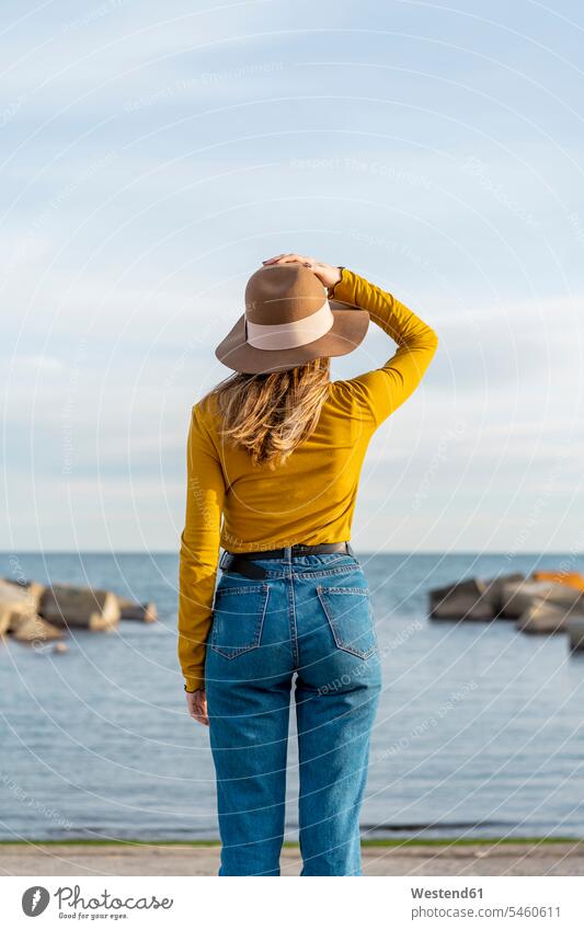 Young woman with arms raised wearing sun hat against sea color image colour image leisure activity leisure activities free time leisure time outdoors