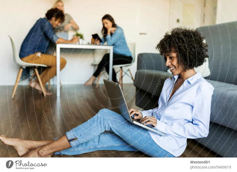 Smiling woman sitting on floor using laptop with friends in background floors Laptop Computers laptops notebook smiling smile females women Seated computer