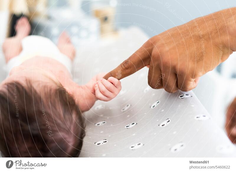Close-up of newborn baby grabbing father's finger on changing table multicultural infants nurselings babies gripping small little Nappy Part Of partial view