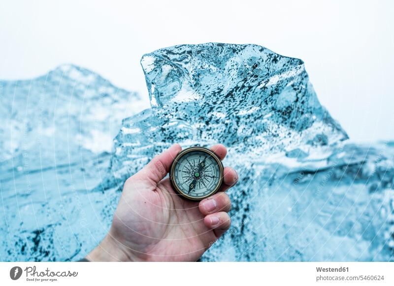 Iceland, Hand of man holding navigational compass in front of large block of ice caucasian caucasian appearance caucasian ethnicity european White - Caucasian
