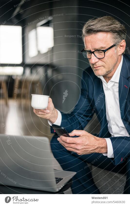 Mature businessman with cup of coffee and laptop using cell phone Coffee Coffee Cup Coffee Cups mobile phone mobiles mobile phones Cellphone cell phones