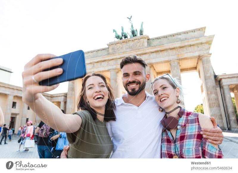 Portrait of three happy friends taking selfie with cell phone in front of Brandenburger Tor, Berlin, Germany touristic tourists cell phones Cellphone mobile